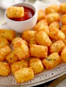 Frozen tator tots in air fryer basket (store bought frozen tater tots are air fried , often served as a side dish) with ketchup in it on the plate