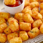 Frozen tator tots in air fryer basket (store bought frozen tater tots are air fried , often served as a side dish) with ketchup in it on the plate