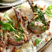 angle shot of lamb chops on an oval platter with basmati rice, mint chimichurri, and toasted pine nuts.