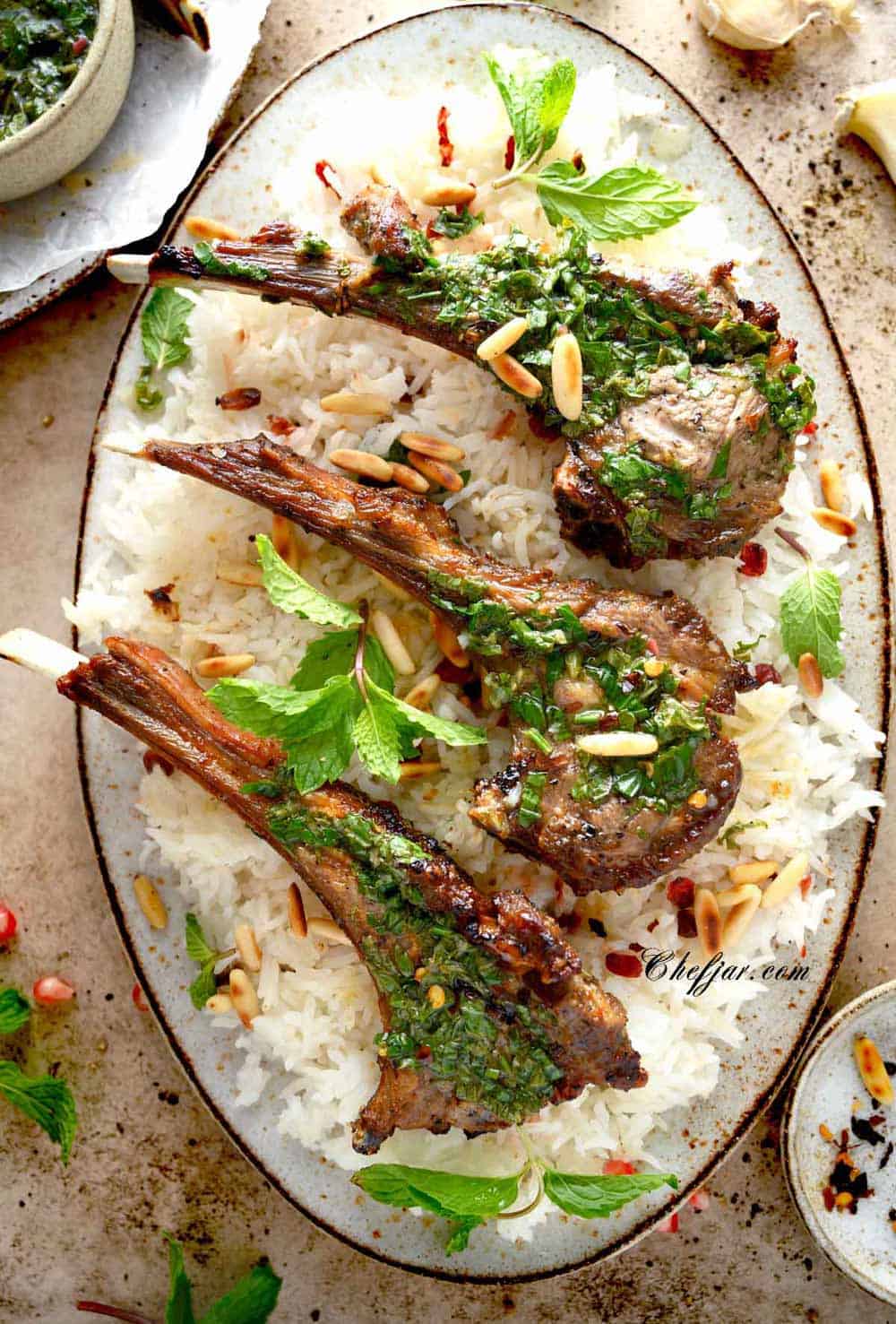 3 lamb chops on an oval platter with basmati rice, mint chimichurri, and toasted pine nuts.