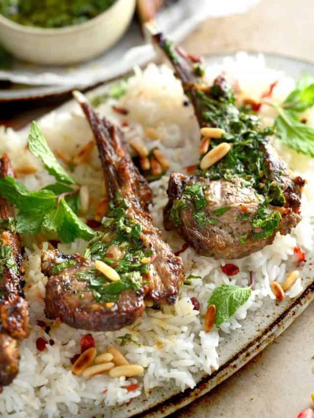 angle shot of lamb chops on an oval platter with basmati rice, mint chimichurri, and toasted pine nuts.