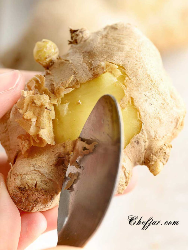 Close up showing how to use a spoon to peel fresh ginger.