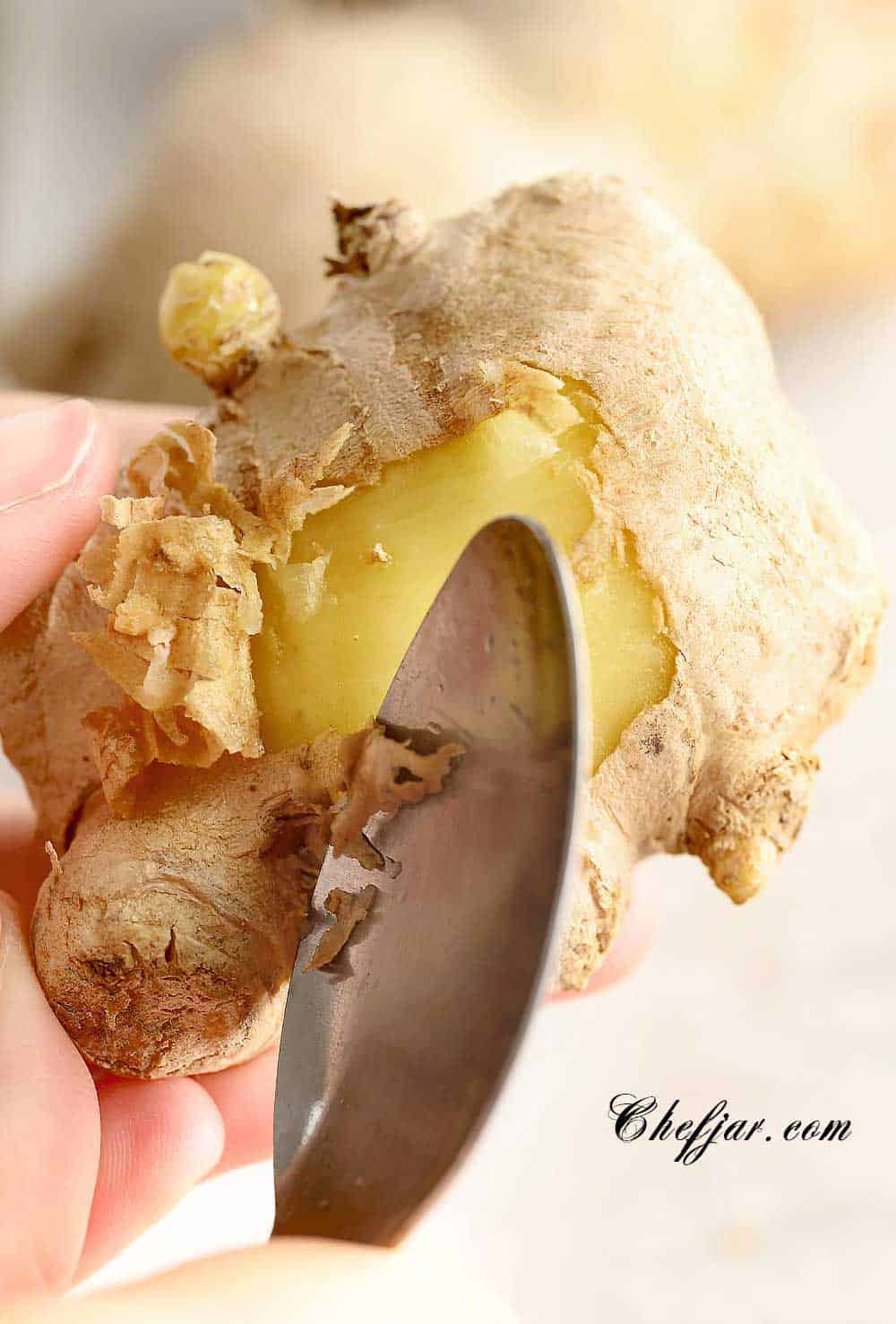 Close up showing how to use a spoon to peel fresh ginger.