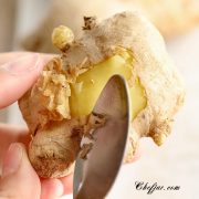 Close up showing how to use a spoon to peel fresh ginger.
