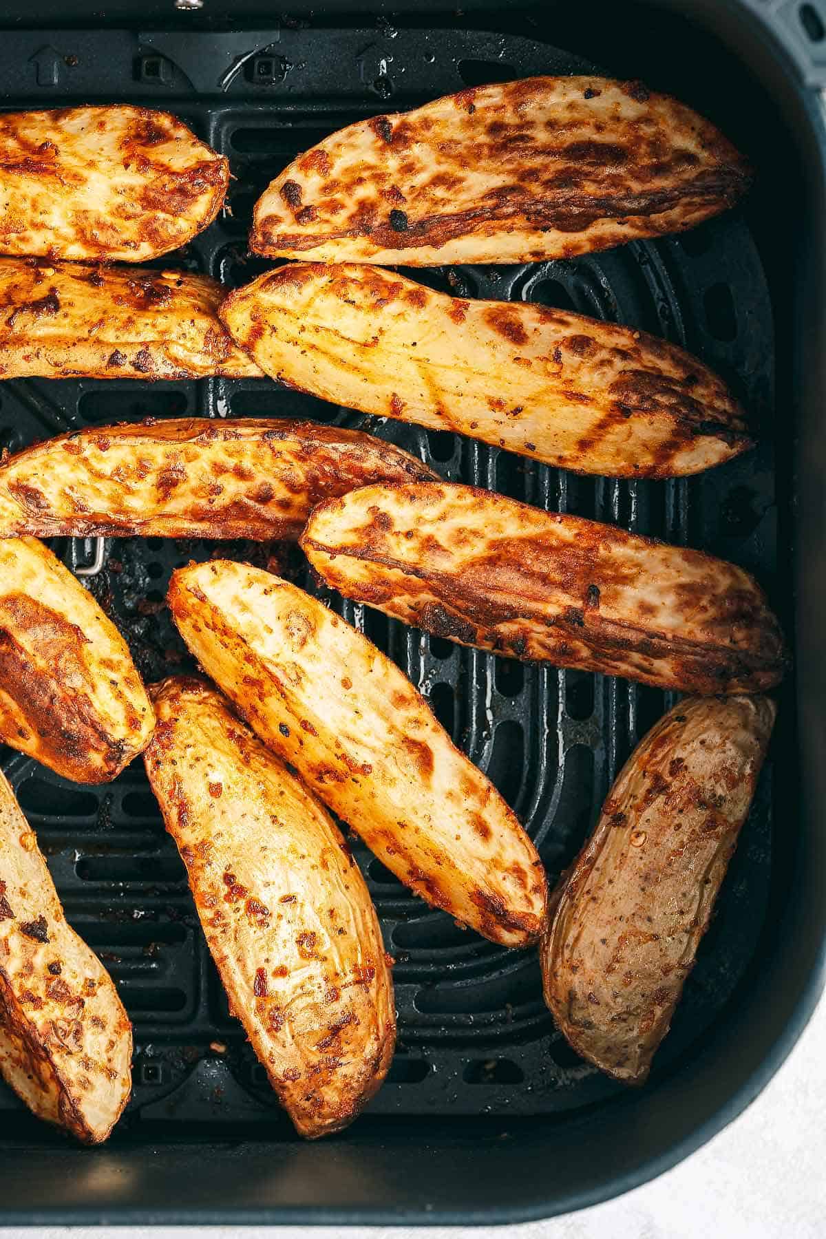 Cooked potato wedges in air fryer basket.