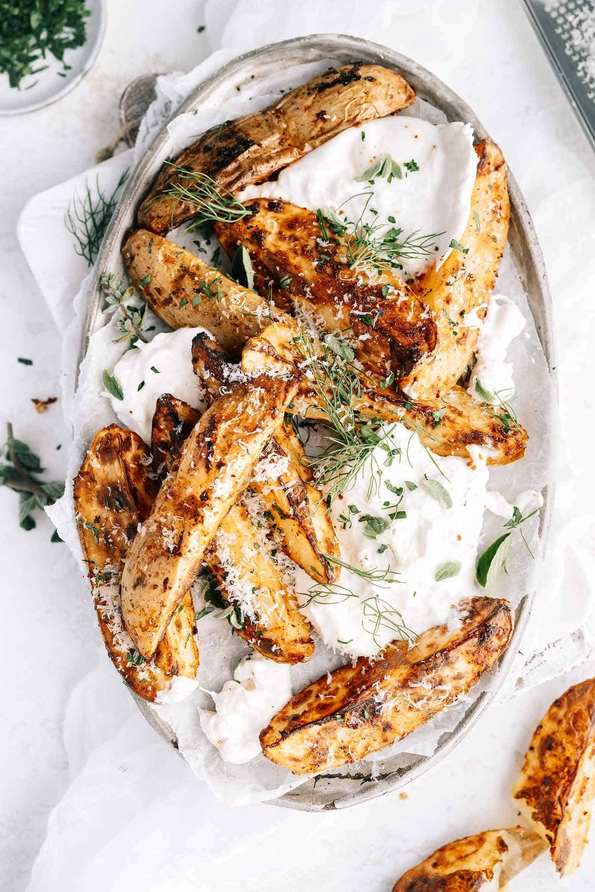 Air fryer potato wedges on a plate, served with burrata cheese, garnished with fresh herbs and sprinkled with parmesan cheese.