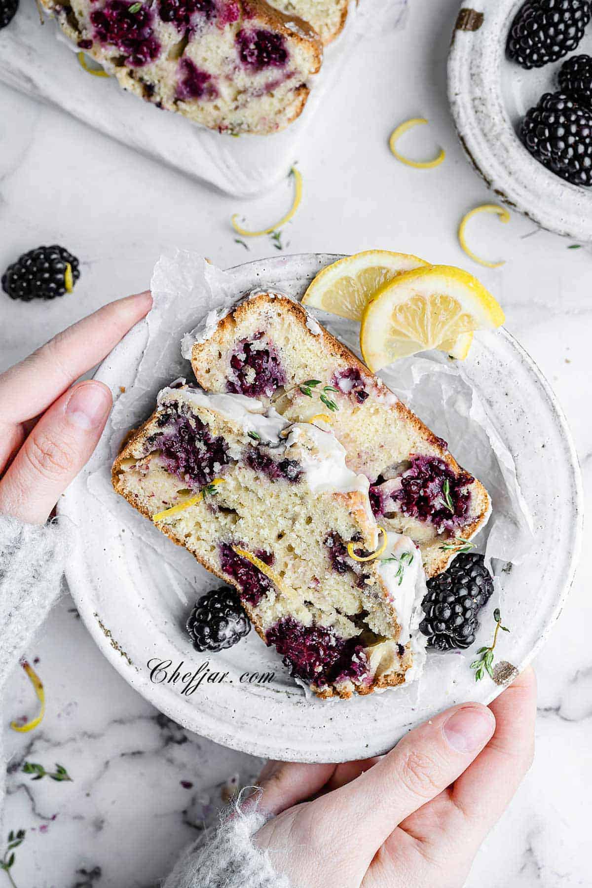 hands holding a plate with two slices of lemon blackberry bread