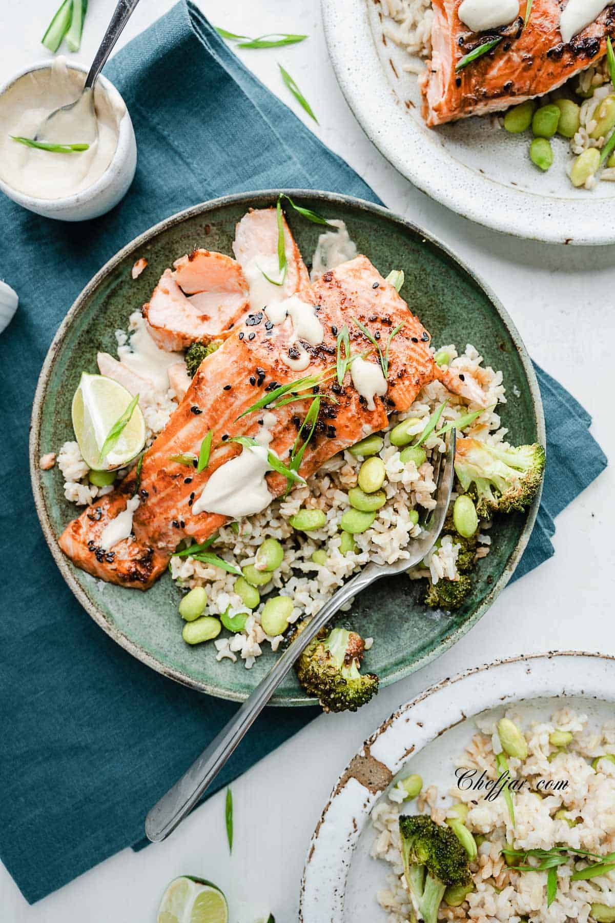 salmon is served on the bed of brown rice with beans and drizzled with tahini dressing.