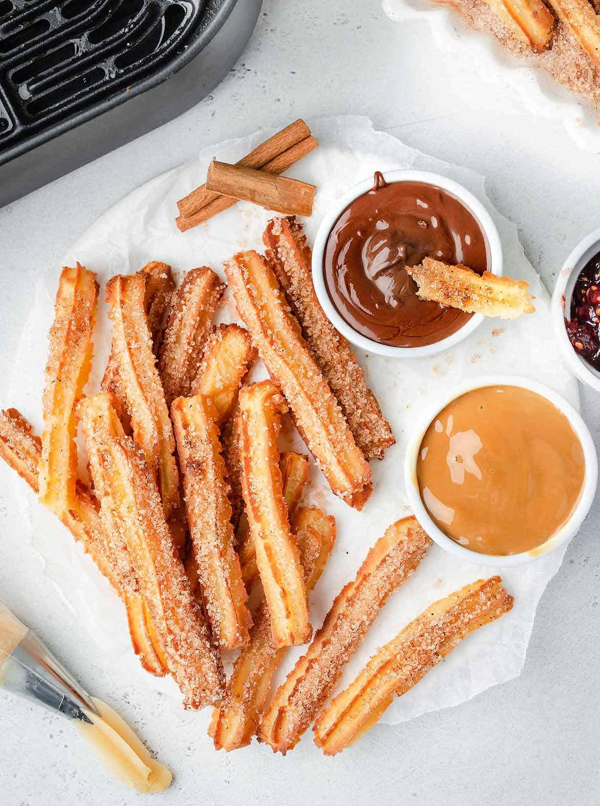 Cinnamon sugar coated churros on a ceramic tray with parchment and two white bowls of nutella and dulce de leche.