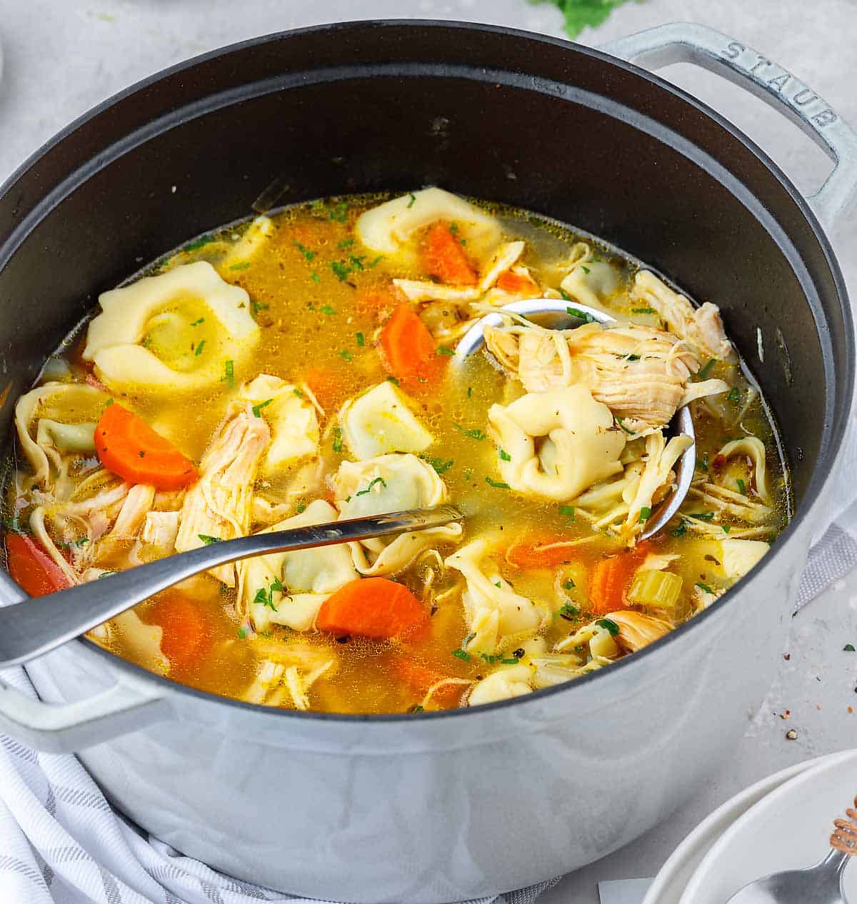 A soup pot filled with Chicken Tortellini Soup with a ladle in it.