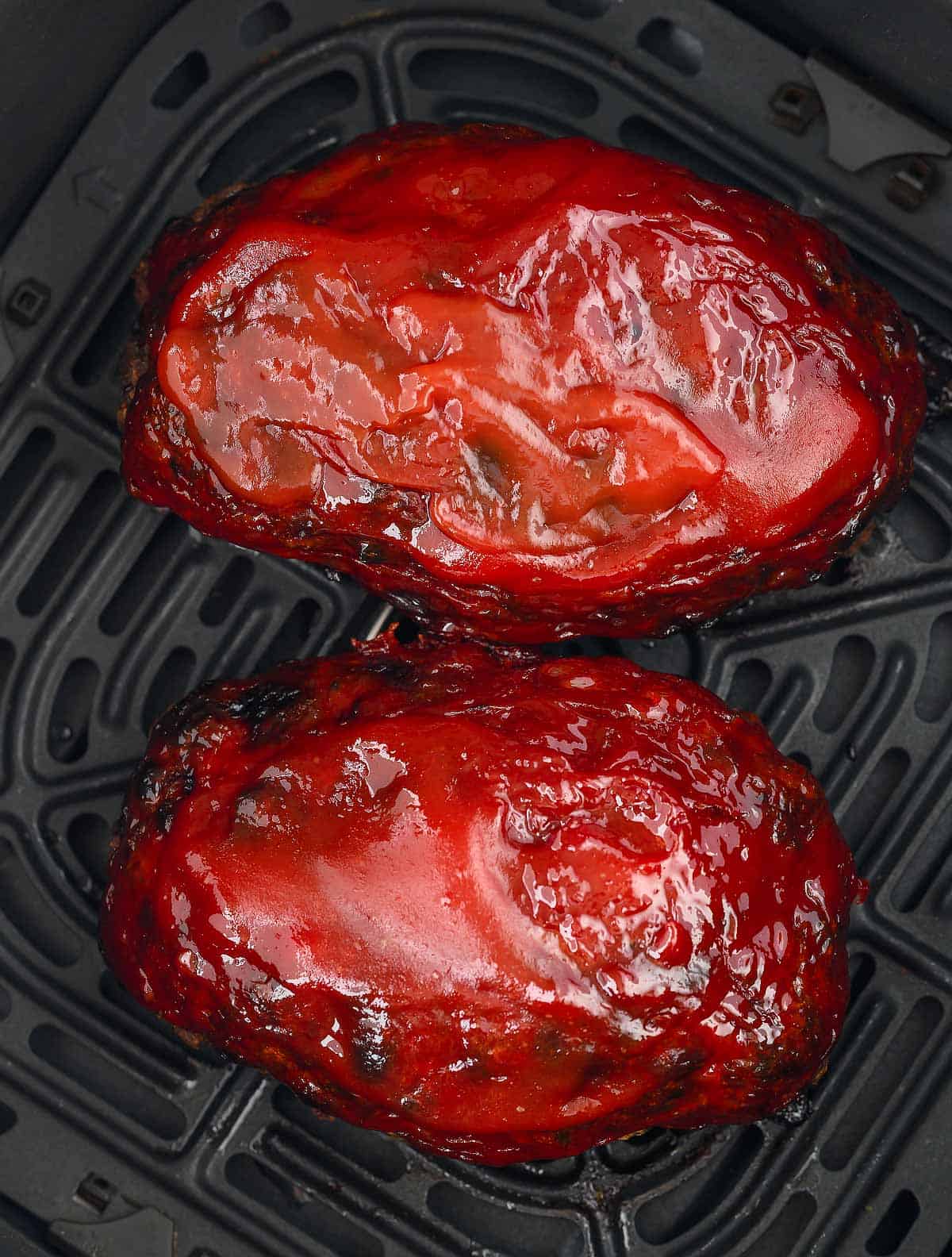 A close up image of two air fryer meatloaves in the air fryer basket