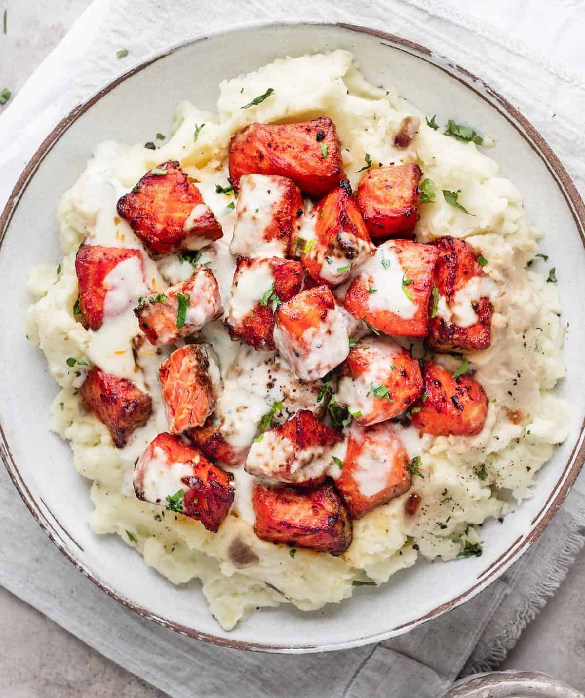 Air fryer salmon bites with garlic cream sauce are served with mashed potatoes.