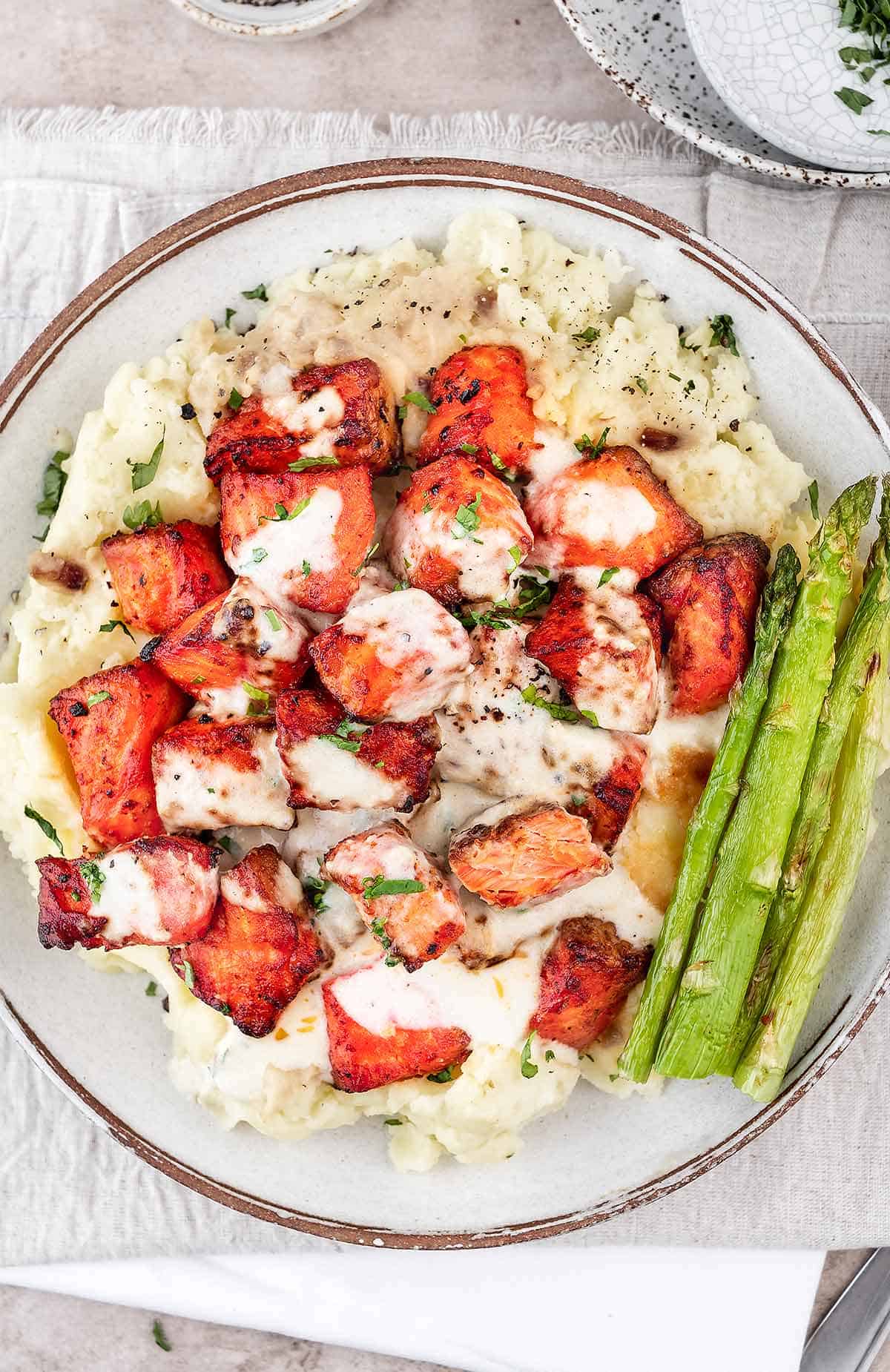 Air fryer salmon with creamy garlic sauce in a white bowl with mashed potatoes and  asparagus.
