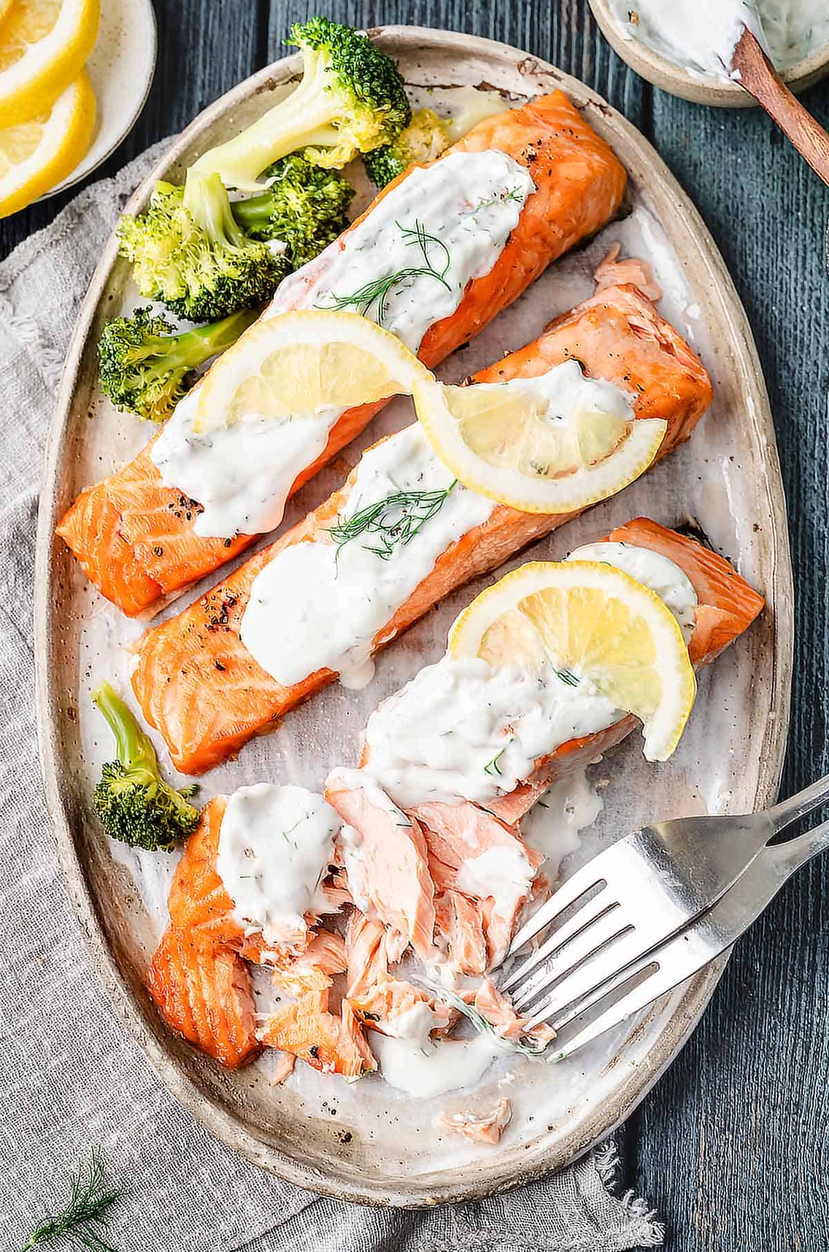 Air fried salmon fillets are topped with a creamy dill sauce and served on a platter with steamed broccoli.