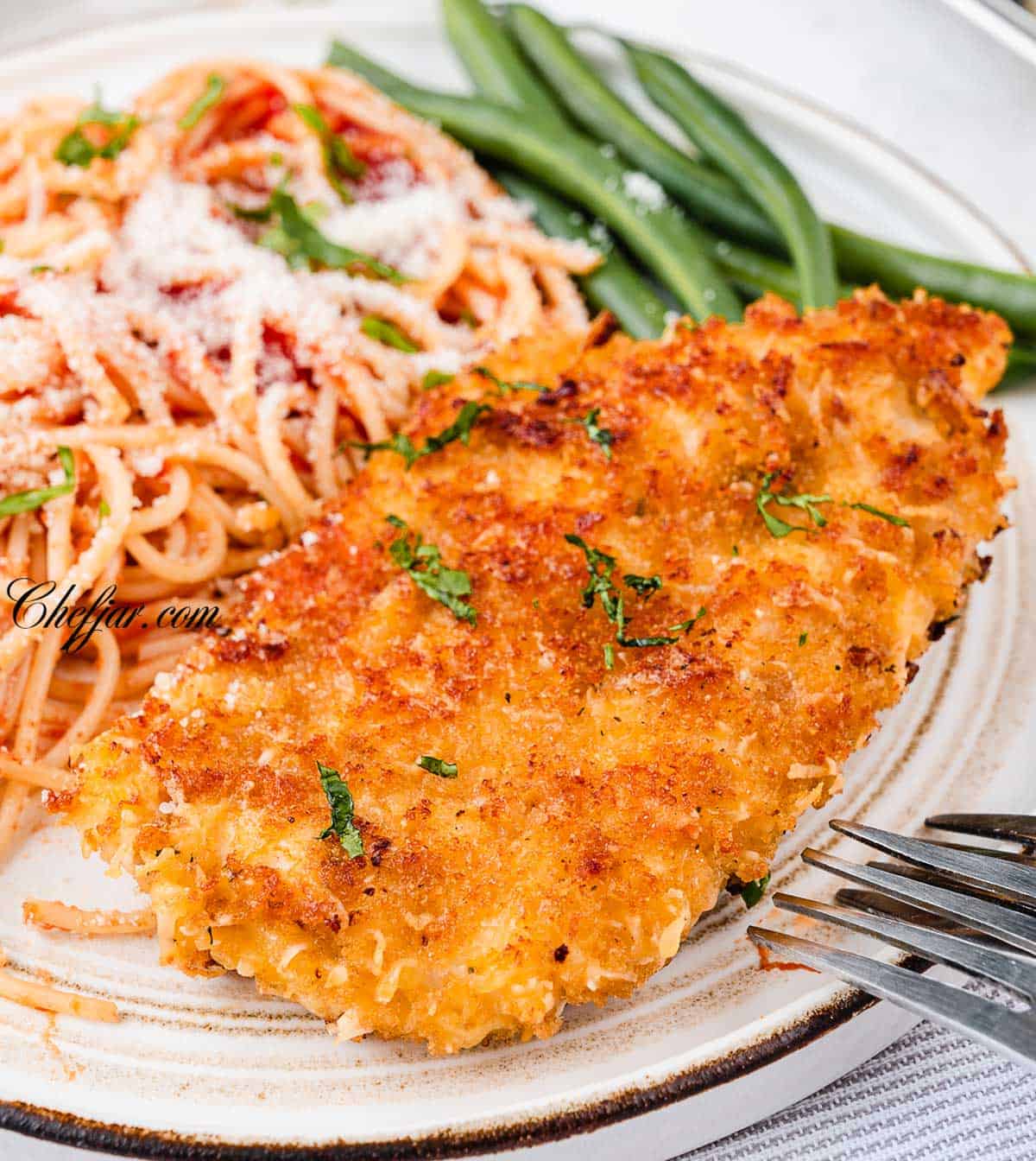 Crusted Chicken Romano on a white plate with spaghetti and creamy tomato sauce
