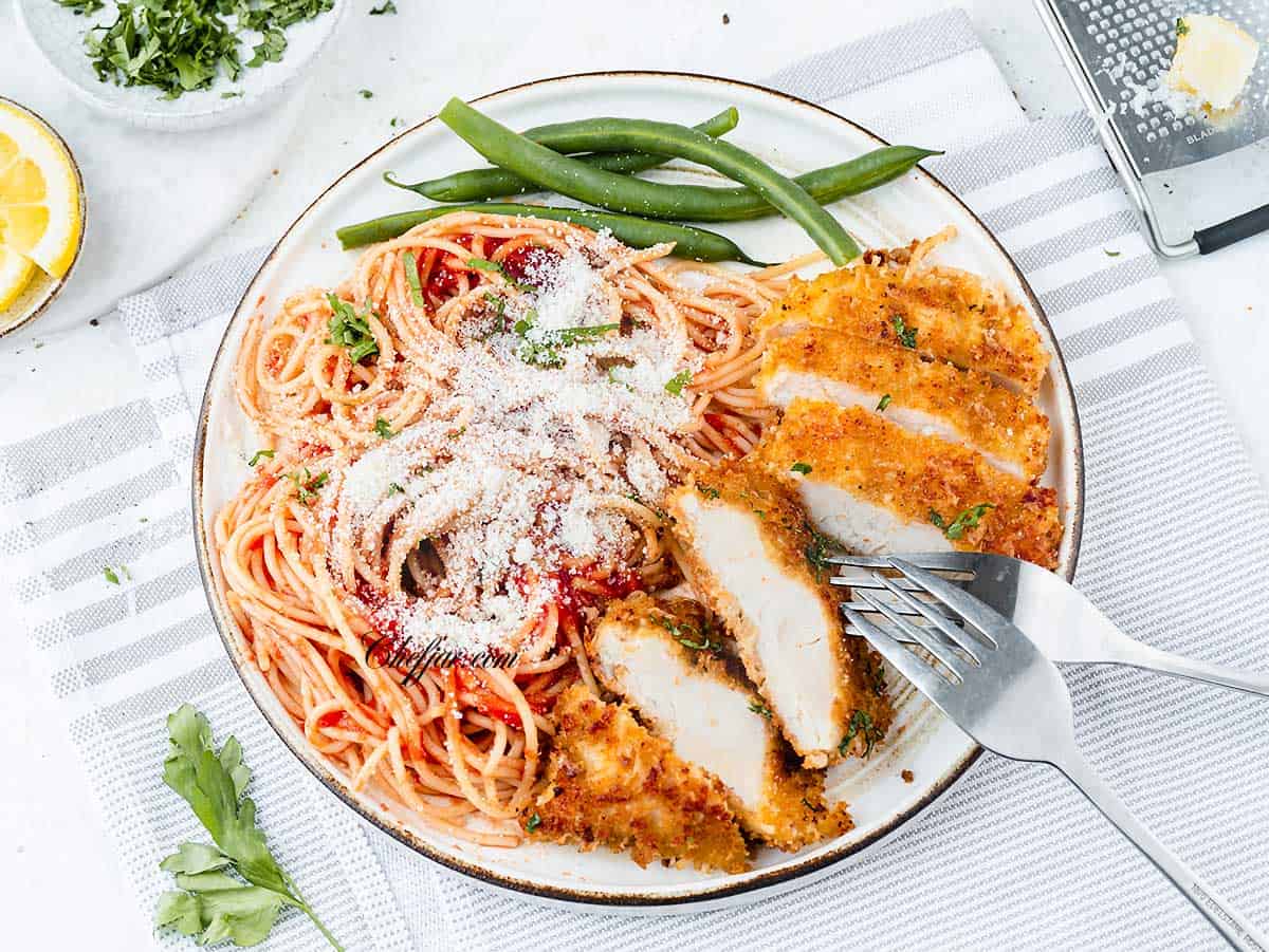 An overhead shot of a plate with crusted chicken Romano and spaghetti with a creamy tomato sauce
