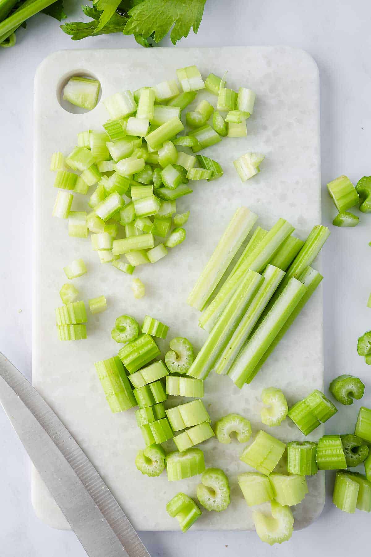 Celery on cutting board being cut into sticks, slices and fine dice
