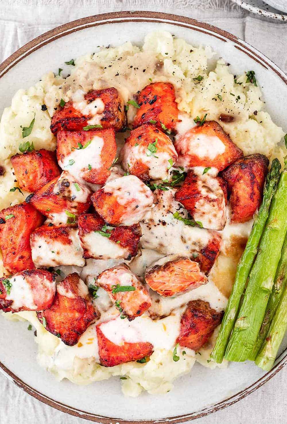 Air fryer salmon with creamy garlic sauce in a white bowl with mashed potatoes and asparagus.