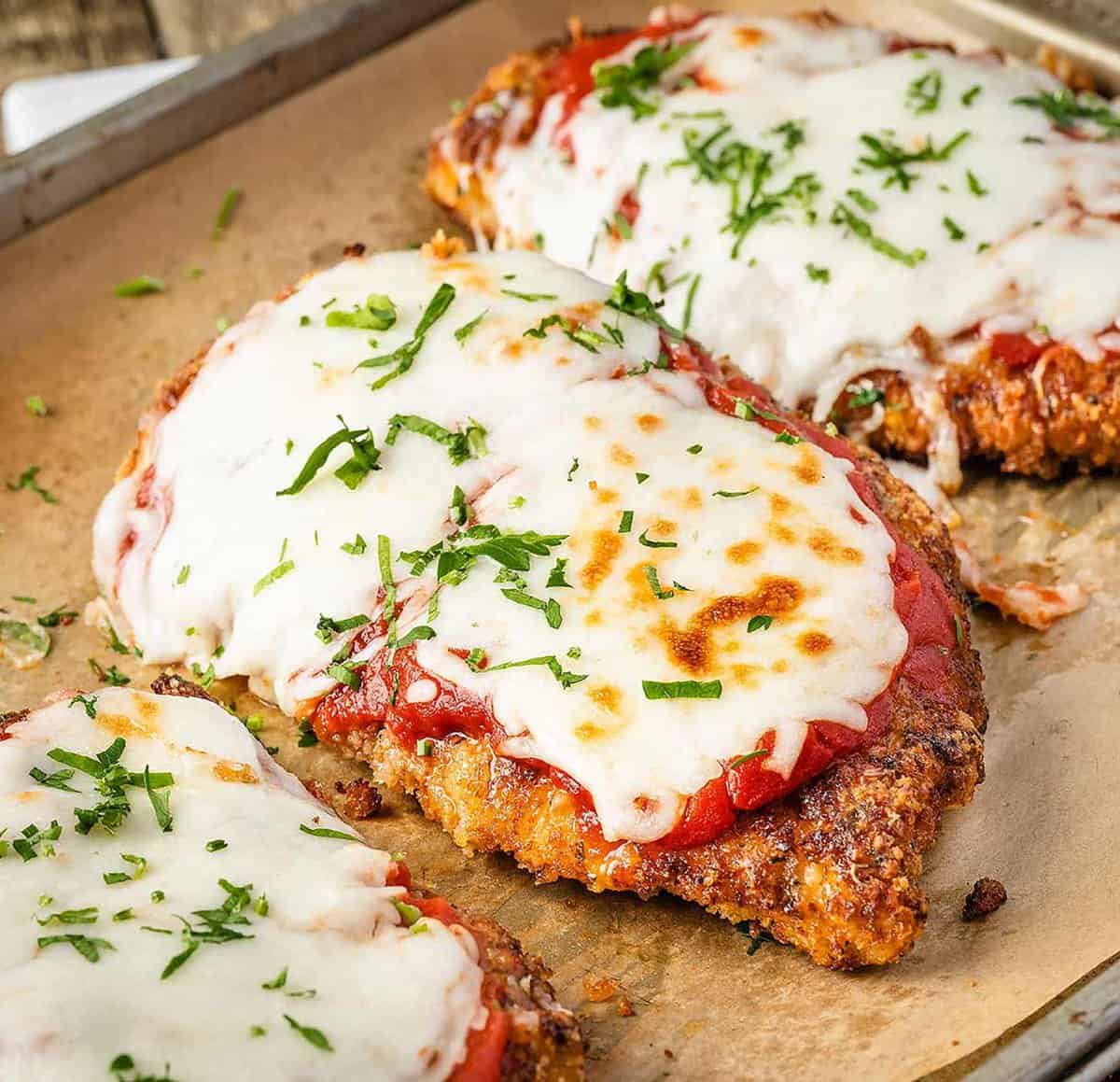 Crispy Chicken Parmesan on a tray with marinara sauce, melted mozzarella, and garnished fresh parsley.