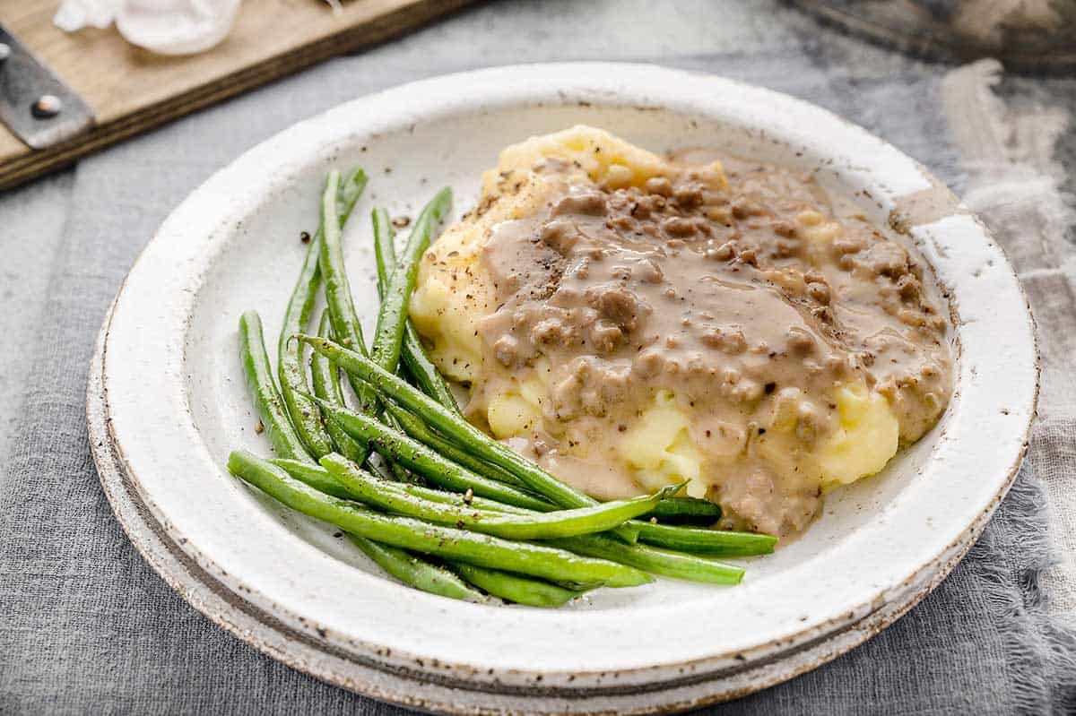 A white plate filled with mashed potatoes that are topped with this easy creamed hamburger gravy recipe / Creamed Hamburger Gravy