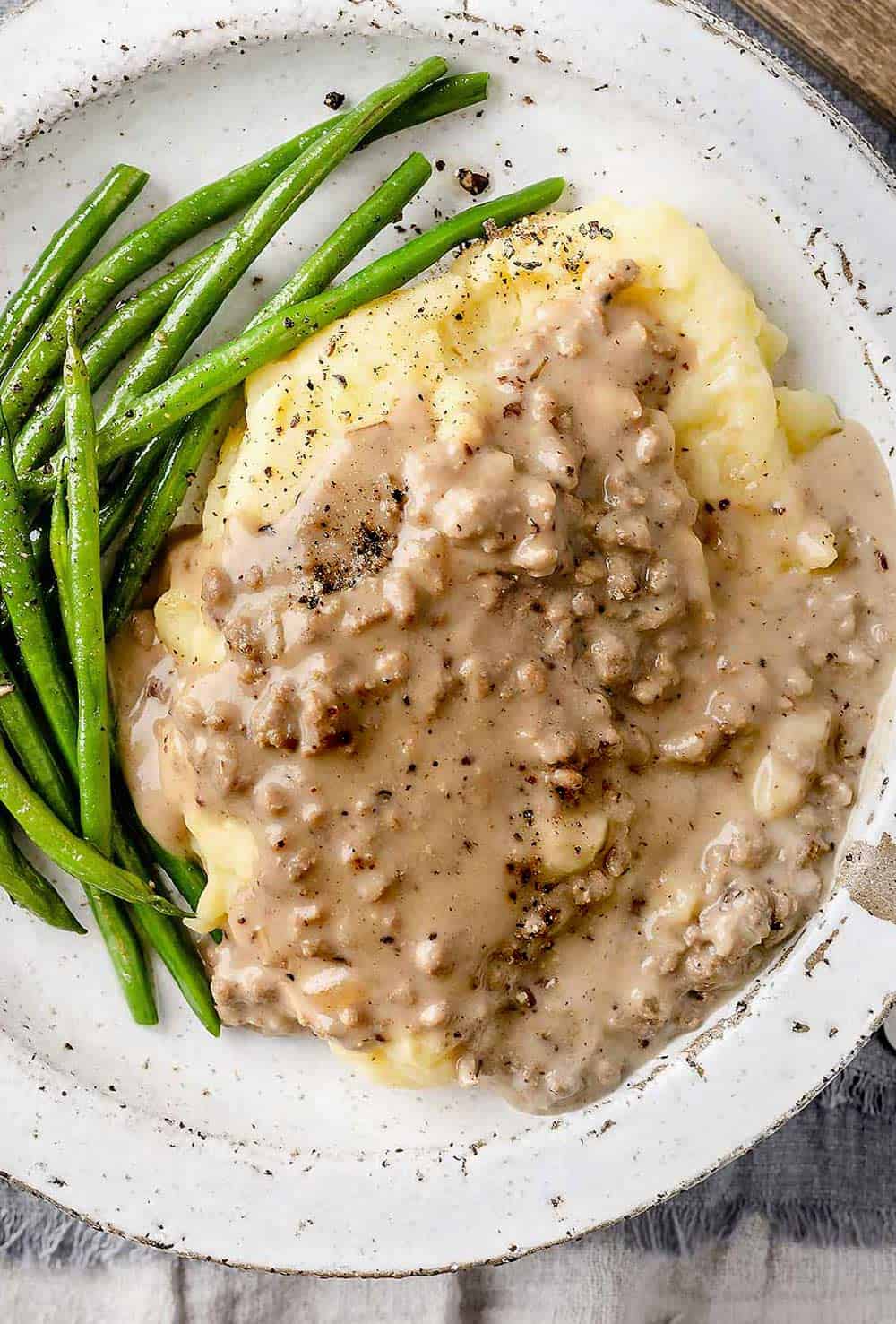 Hamburger gravy on a plate with mashed potatoes and sautéed green beans.
