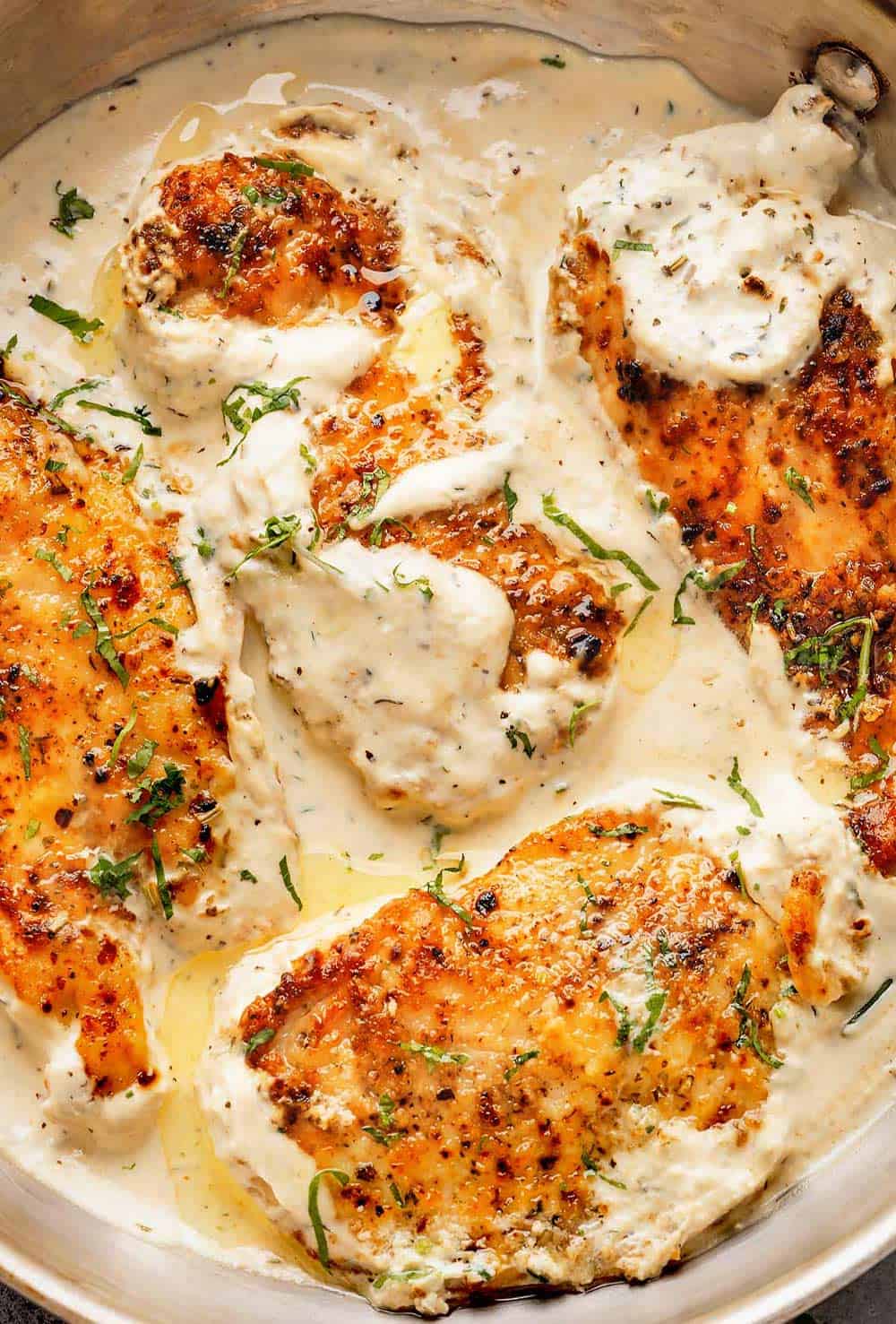A skillet filled with Herb Chicken in a cream sauce with fresh parsley and rosemary./