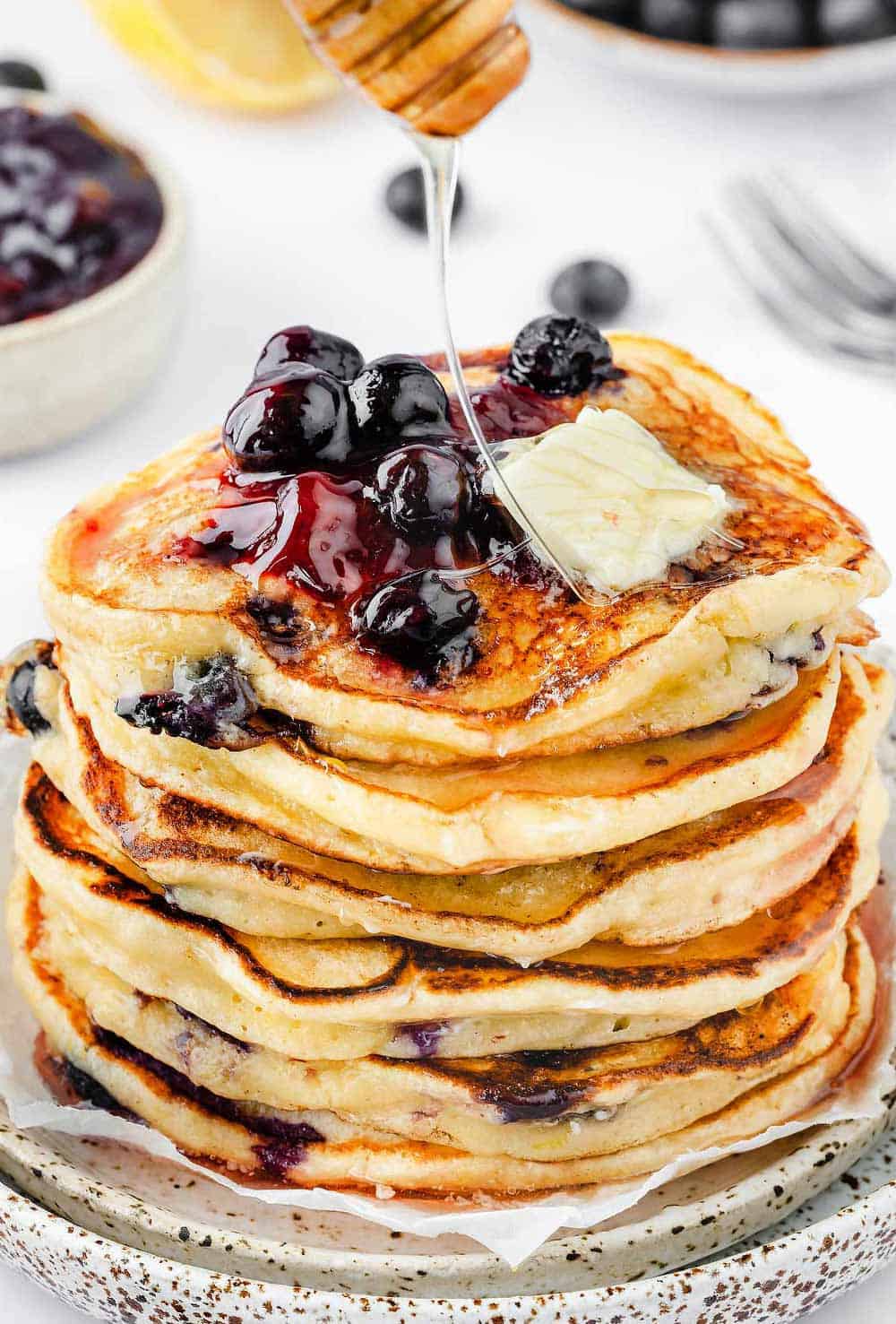 A stack of lemon blueberry ricotta pancakes with honey being drizzled over them / Lemon Blueberry and Ricotta Pancakes