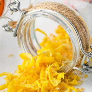 An image of a jar of dried lemon peel that has been tipped over, with some of the dried lemon zest spilled out onto a white surface.