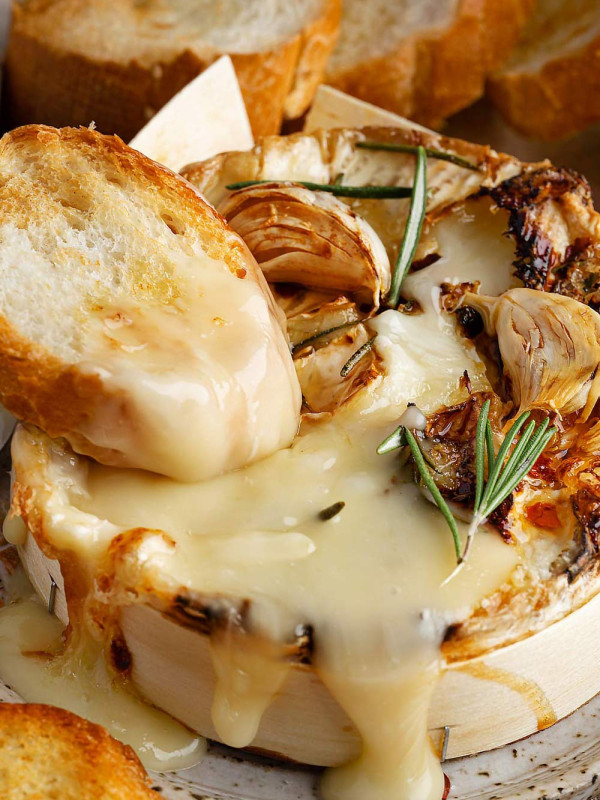 Crusty bread dipped into a melted wheel of Camembert cheese on a plate.