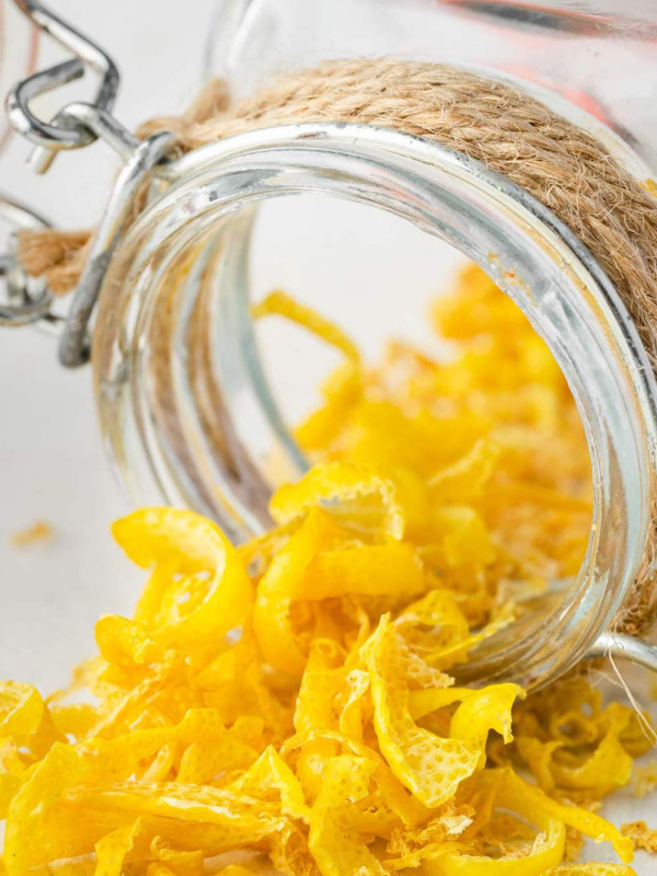 An image of a jar of dried lemon peel that has been tipped over, with some of the dried lemon zest spilled out onto a white surface.