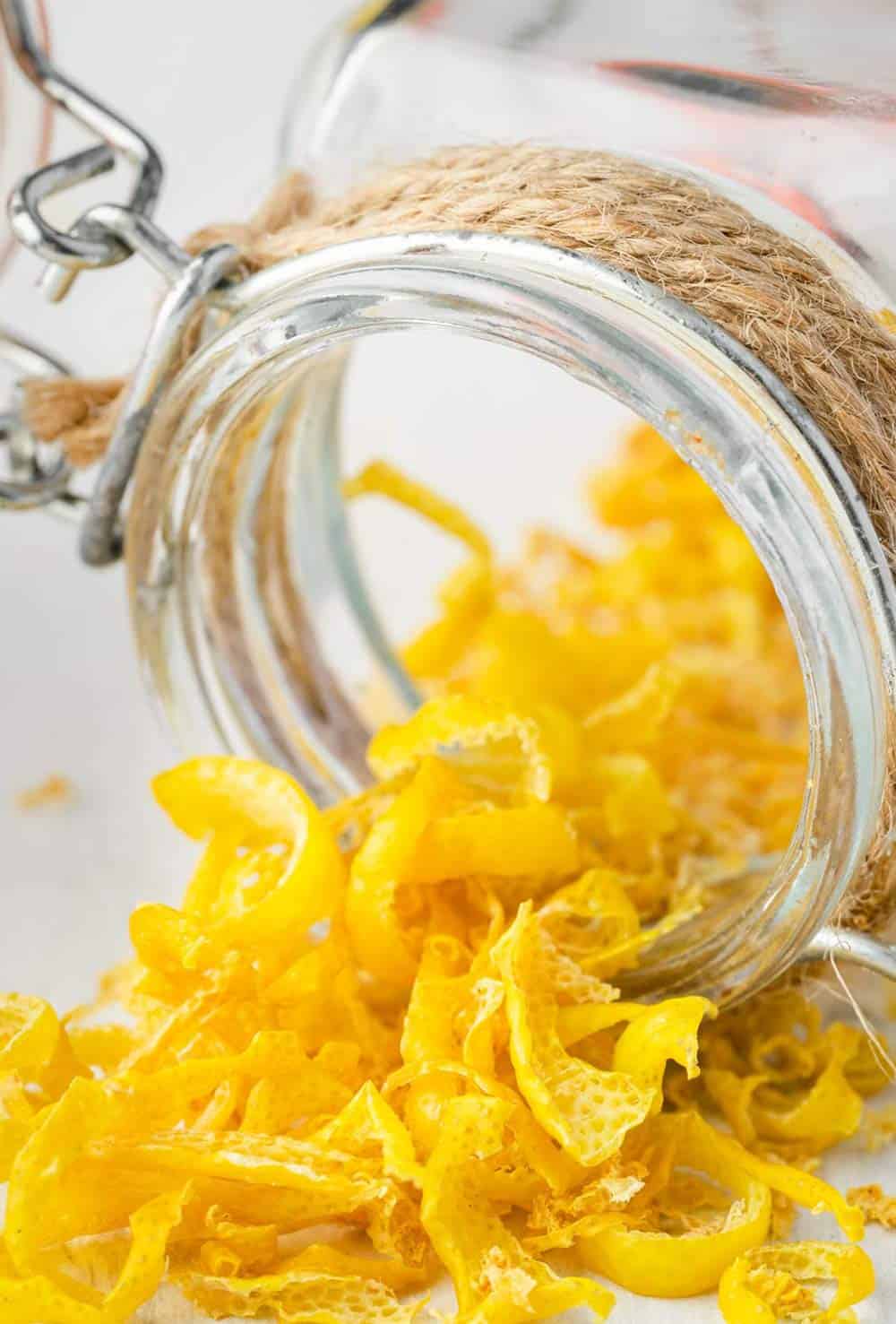 An image of a jar of dried lemon peel that has been tipped over, with some of the dried lemon zest spilled out onto a white surface.