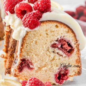 Slice of Lemon Raspberry Bundt Cake on a white plate with fresh raspberries and lemon slices on top.