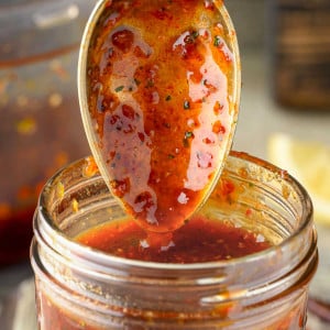 BBQ sauce being poured from a spoon into a Mason jar.
