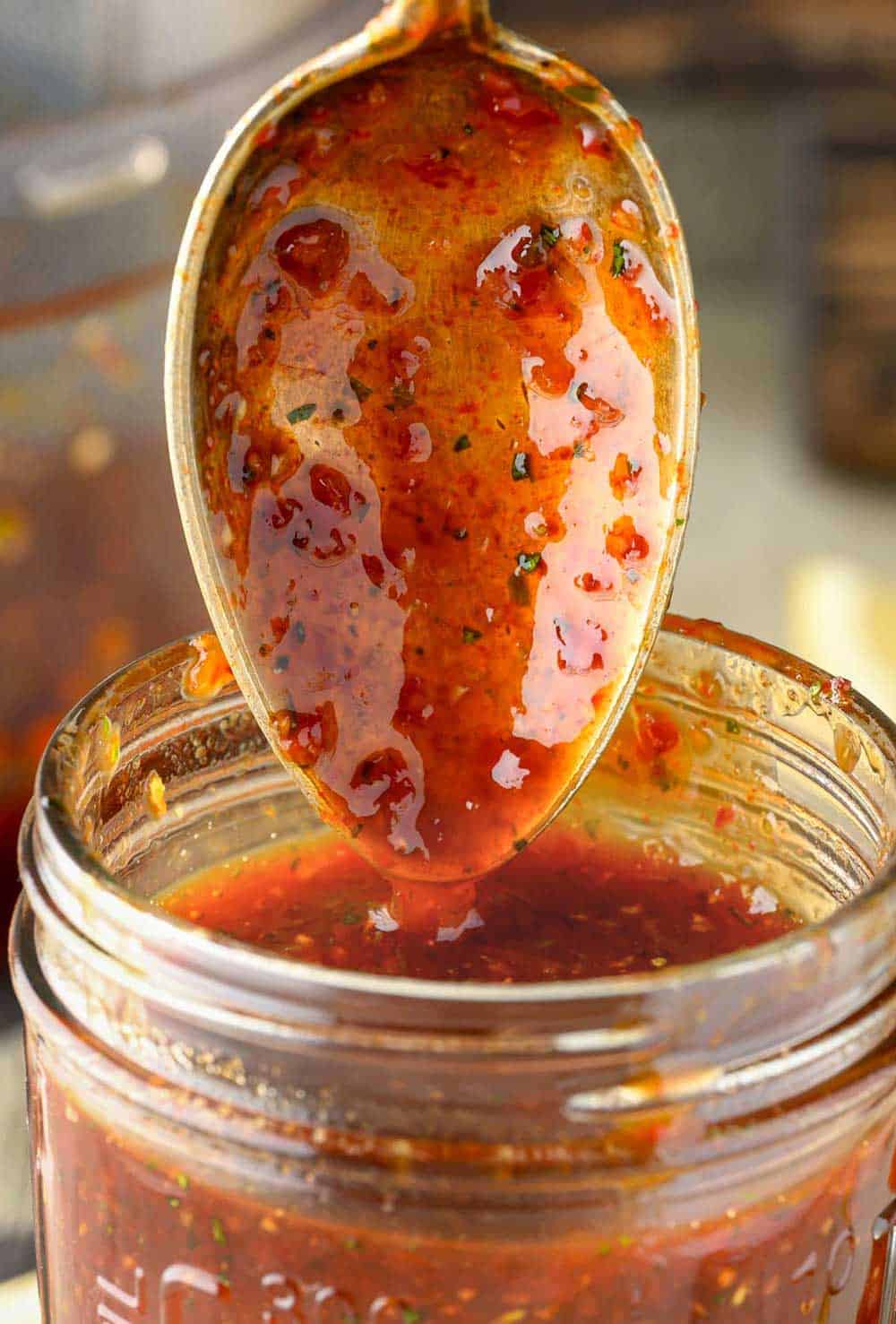 BBQ sauce being poured from a spoon into a Mason jar.