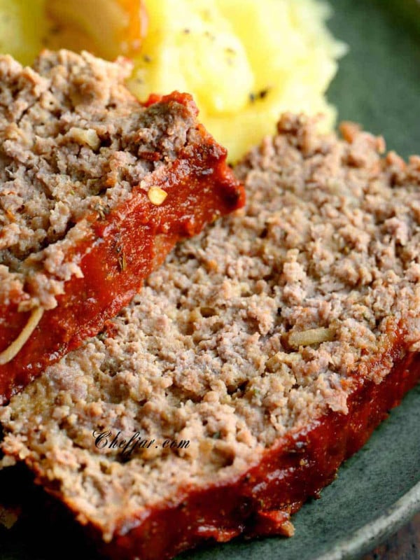 Image of a slice of savory meatloaf topped with a tangy tomato glaze, served on a plate next to a generous portion of creamy mashed potatoes with a sprinkle of fresh herbs on top.