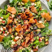 Fattoush salad in a large grey bowl with pita bread chips and pomegranate molasses, served with two forks on the side.