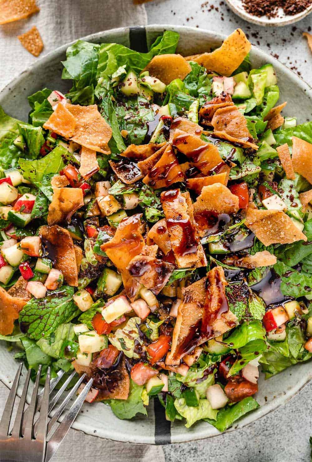 Fattoush Salad served in a large grey bowl, topped with crispy pita bread chips and drizzled with sweet and tangy pomegranate molasses dressing.