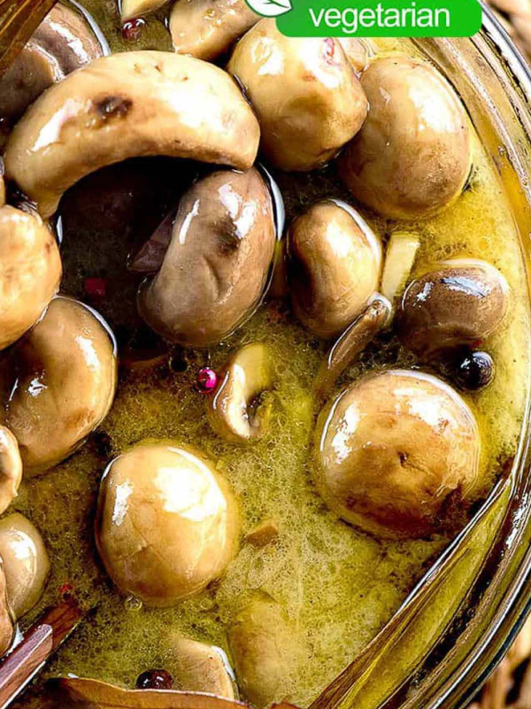 Overhead image of a glass bowl filled with marinated mushrooms in marinade. The mushrooms are brown and glossy, and the marinade contains visible herbs and spices.