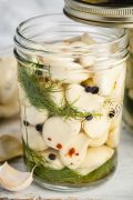 Image of a wide mouth Kilner jar filled with pickled garlic cloves. The garlic cloves are submerged in a light-colored vinegar brine and are visible through the clear glass jar.