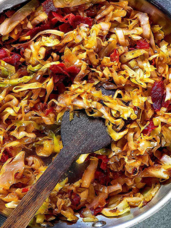 Fried cabbage in a skillet with crispy bacon.