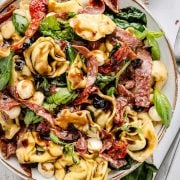 Image of a fresh and colorful Tuscan Salad in a white bowl, topped with a tangy balsamic vinaigrette. In the background, a small bowl of sun-dried tomatoes adds an extra burst of flavor.