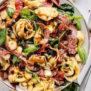Image of a fresh and colorful Tuscan Salad in a white bowl, topped with a tangy balsamic vinaigrette. In the background, a small bowl of sun-dried tomatoes adds an extra burst of flavor.