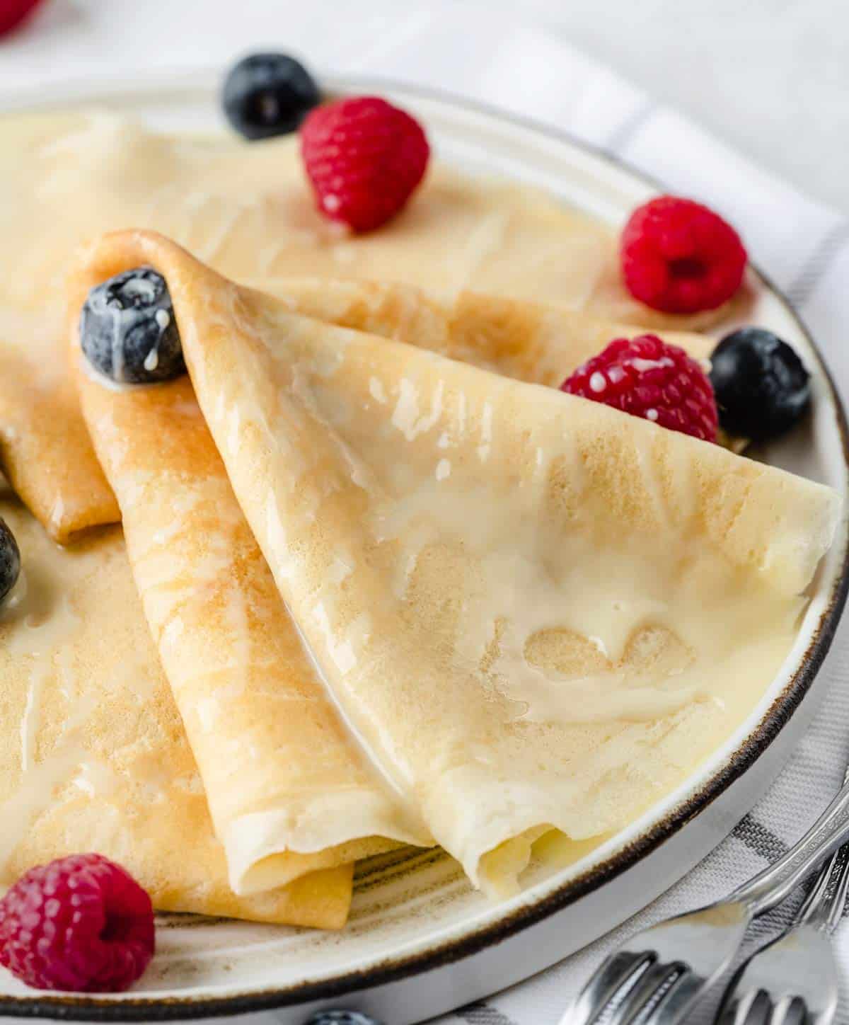 Close-up view of crepes drizzled with condensed milk with blueberries and raspberries.