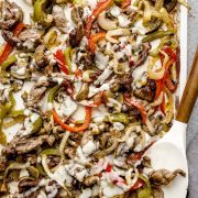 Baked Philly cheesesteak on a baking sheet, drizzled with homemade provolone cheese sauce and roasted vegetables.