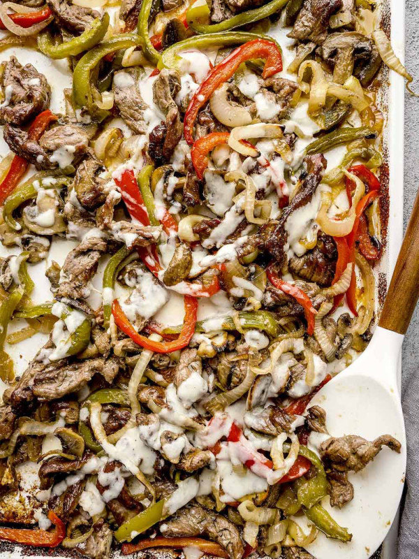 Baked Philly cheesesteak on a baking sheet, drizzled with homemade provolone cheese sauce and roasted vegetables.