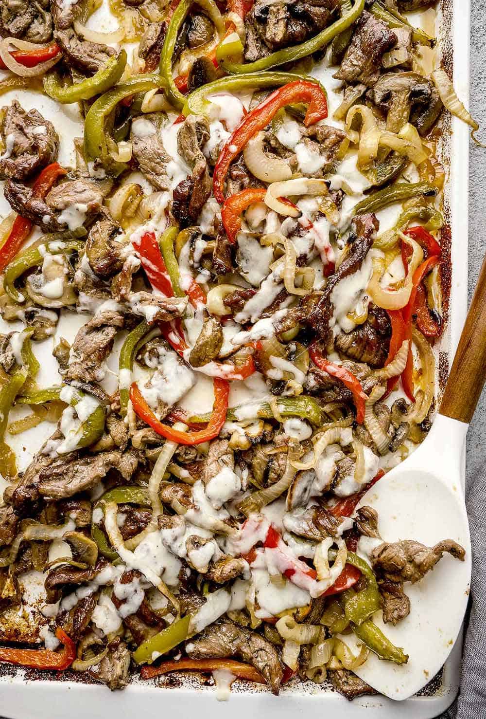 Baked Philly cheesesteak on a baking sheet, drizzled with homemade provolone cheese sauce and roasted vegetables.