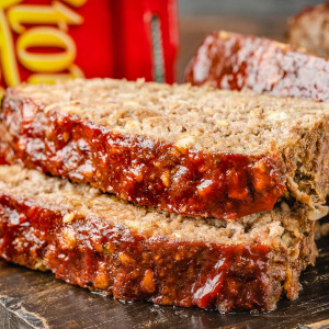 The image shows two slices of Stove Top stuffing meatloaf placed on a wooden board. In the background, there is a box of Stove Top stuffing mix.