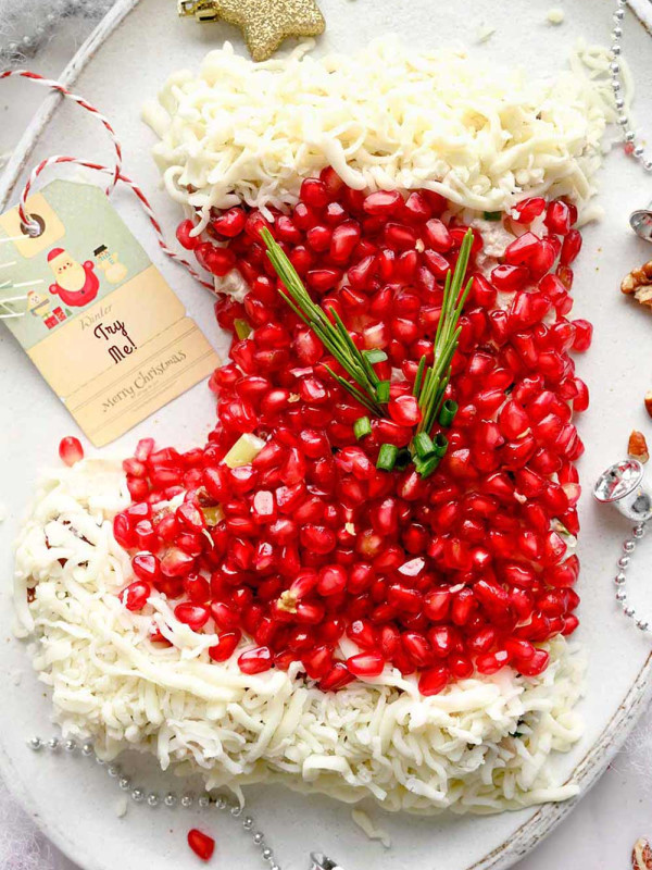 A festive Christmas Chicken Salad arranged in the shape of a stocking on a white plate. The salad features diced chicken, pecans, celery, mozzarella cheese, green onions, and pomegranate arils, and mayo dressing.