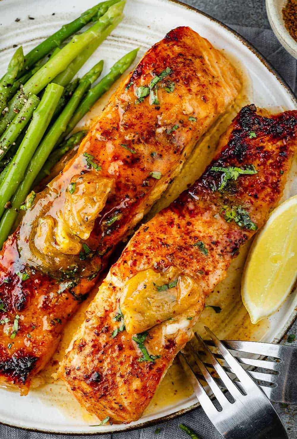 Two succulent pieces of Cajun Honey Butter Salmon served on a plate alongside vibrant asparagus spears.