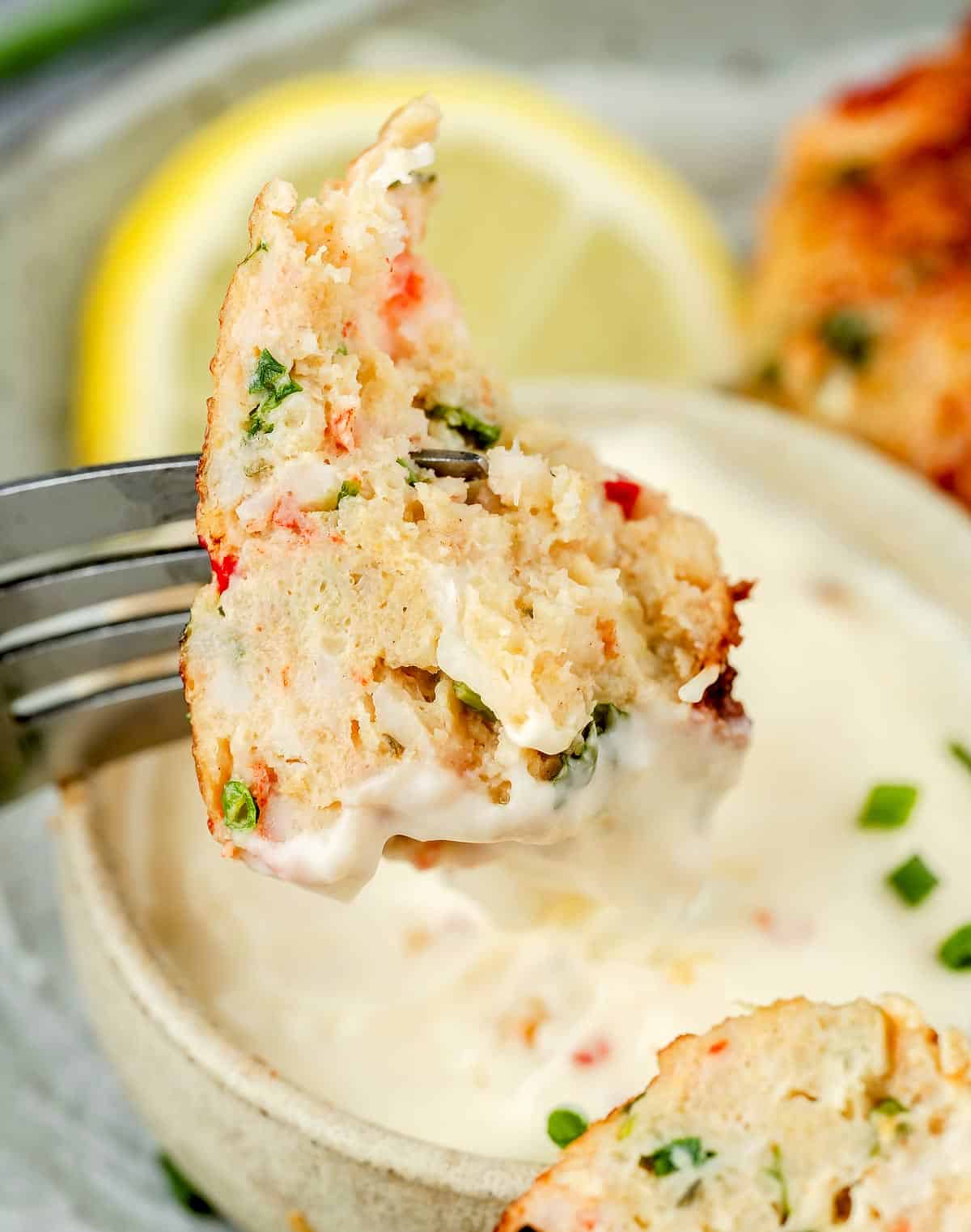 A succulent shrimp cake piece on a fork, tantalizingly dipped in flavorful lime-chili mayo